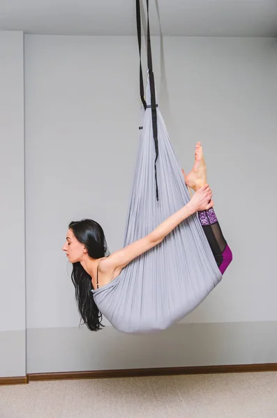 slim, fit yoga trainer does fly yoga in a hammock in the studio.