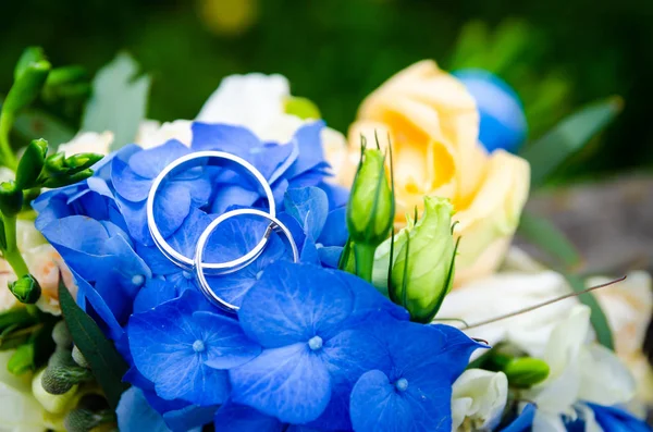 Coppia di fedi nuziali sullo sfondo del bouquet nuziale — Foto Stock