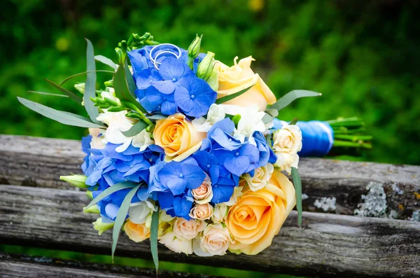 Dvojice svatebních prstenců na pozadí svatební kytice — Stock fotografie