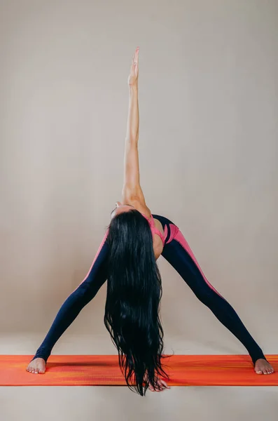 Hermosa mujer en forma slim entrenador se encuentra en asanas sobre una alfombra brillante — Foto de Stock