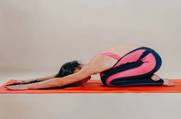 Hermosa mujer en forma slim entrenador se encuentra en asanas sobre una alfombra brillante — Foto de Stock