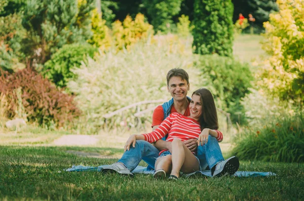 Jeune couple amoureux est assis sur un plaid dans le parc, étreignant , — Photo