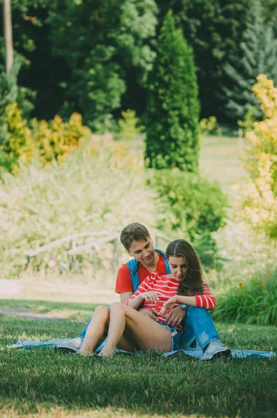 Young loving couple is sitting on a plaid in the park, hugging, — Stock Photo, Image
