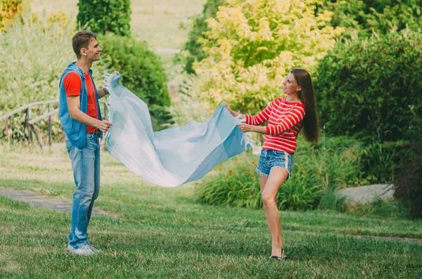 Una pareja joven y cariñosa extiende una manta a cuadros en un prado en el parque. Pic — Foto de Stock
