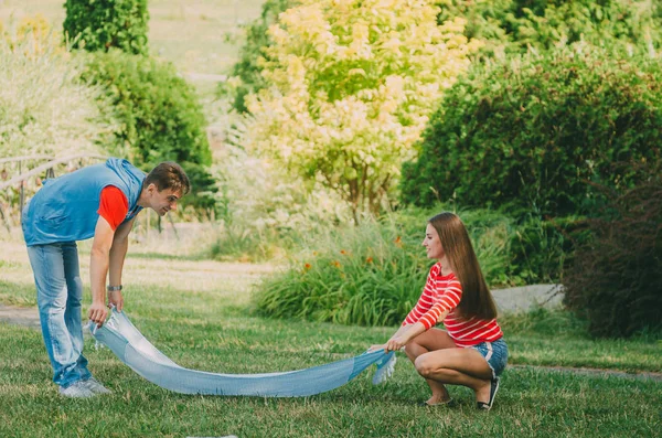 Un jeune couple amoureux déploie un plaid sur une prairie du parc. Pic — Photo