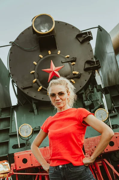 一个戴着圆圆的时髦眼镜的女人站在一列火车前面。 自我- — 图库照片