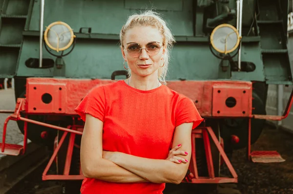 Woman in round stylish glasses stands in front of a train. Self- — Stock Photo, Image