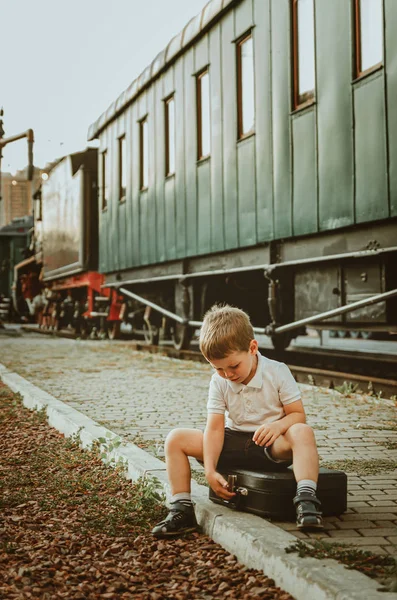 Vacaciones con niños. Un chico se sienta en una maleta en la plataforma — Foto de Stock