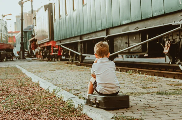 Liburan dengan anak-anak. Seorang anak laki-laki duduk di sebuah koper di atas panggung — Stok Foto
