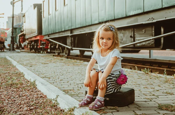 A girl sits on a suitcase on the platform at the station near th — Stock Photo, Image