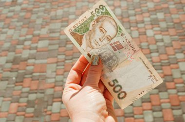 Kadın eli, arka planda 500 Hryvnia banknotu tutuyor.