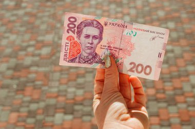 Kadın eli, arka planda 200 Hryvnia banknotu tutuyor.