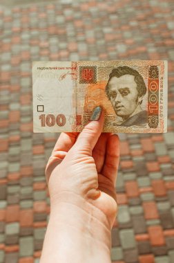 Kadın eli, arka planda 100 Hryvnia banknotu tutuyor.