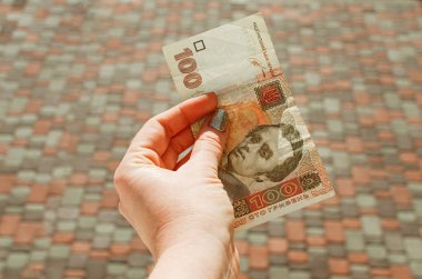 Kadın eli, arka planda 100 Hryvnia banknotu tutuyor.
