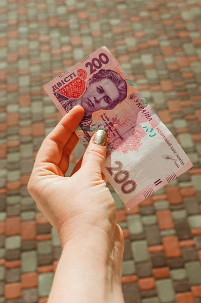 Mano femenina sostiene un billete de 200 hryvnia sobre un fondo de calle — Foto de Stock