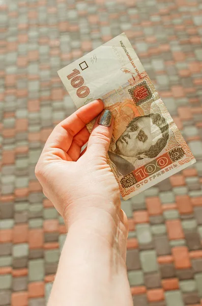 Mano femenina sostiene un billete de 100 hryvnia sobre un fondo de calle — Foto de Stock