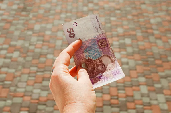 Mano femenina sostiene un billete de 50 hryvnia sobre un fondo de calle . — Foto de Stock