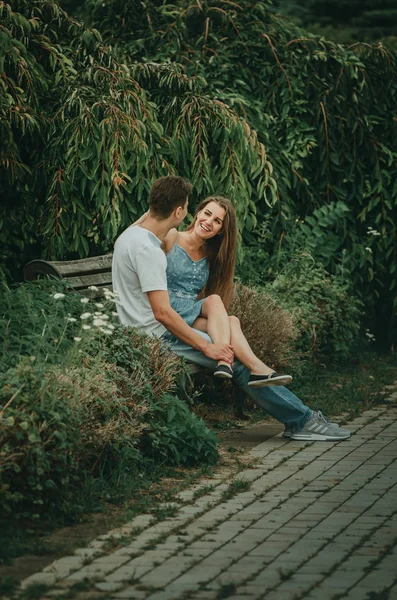 Belo casal apaixonado senta-se em um parque em um banco no verão — Fotografia de Stock