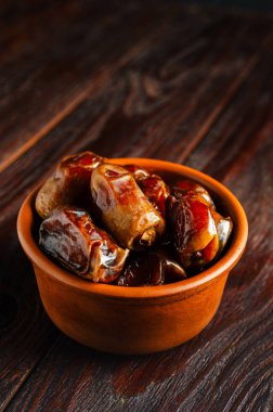 Ahşap bir masanın üzerinde kurumuş hurma olan kil kahverengi bir kase. Sağlıklı tatlı.