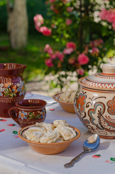 Homemade pierogi in clay ethnic Ukrainian dishes on a table in the summer garden. National cuisine, lifestyle