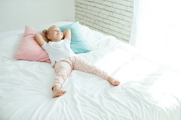En liten flicka i sängen med vitt linne. Ett barn hemma på morgonen vaknar upp i sitt rum. — Stockfoto