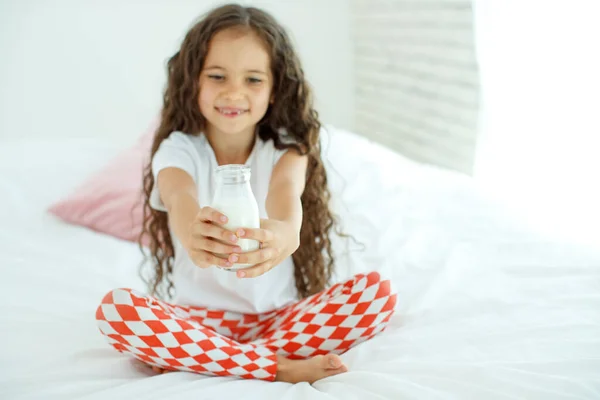 Il bambino sta bevendo latte. Una bambina a casa sul letto beve yogurt. — Foto Stock