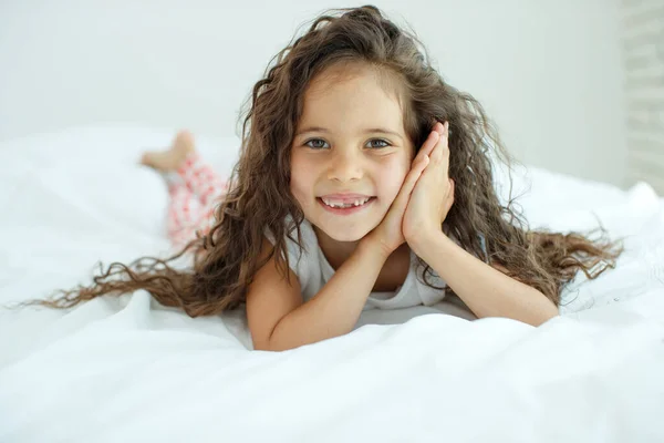 Niña en la cama. El niño en casa se despierta en la cama por la mañana. — Foto de Stock