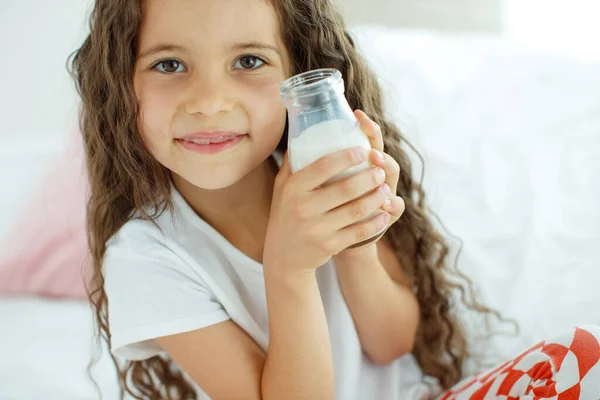 Il bambino sta bevendo latte. Una bambina a casa sul letto beve yogurt. — Foto Stock