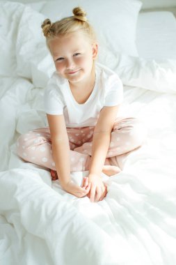 Beyaz çarşaflarla yatakta küçük bir kız. Sabah evde bir çocuk uyanır odasında..