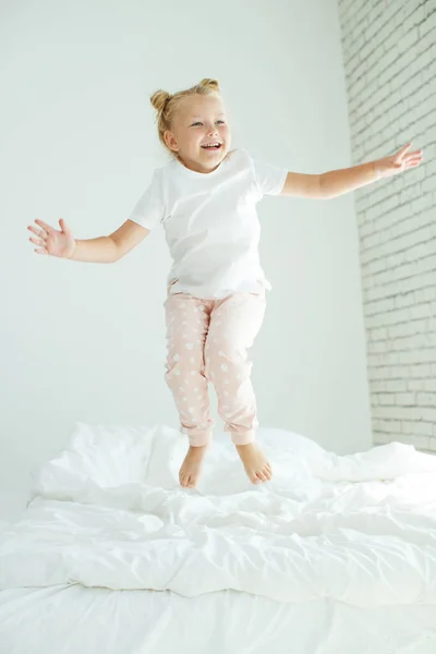 Kleines Mädchen im Bett mit weißer Wäsche. Ein Kind wacht morgens zu Hause in seinem Zimmer auf. — Stockfoto