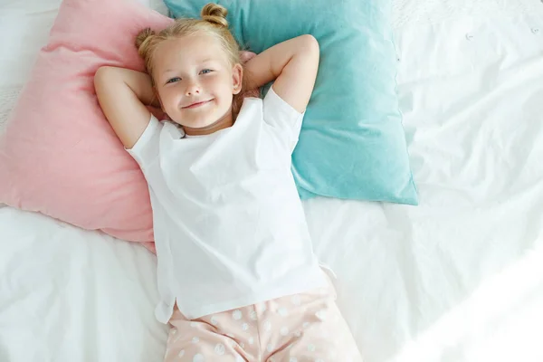 白いリネンのベッドで小さな女の子。朝家にいる子供が部屋で目を覚ます. — ストック写真