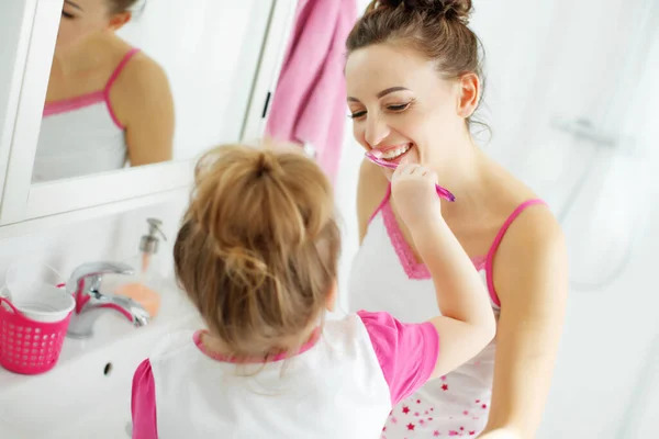 Мама з донькою чистять зуби зубними щітками у ванній кімнаті. Мама і маленька дівчинка в домашньому одязі.. — стокове фото