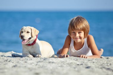 Mutlu çocuk mavi gökyüzüne karşı deniz kıyısında köpeğiyle oynuyor. En iyi arkadaşlar tatilde eğlenir..