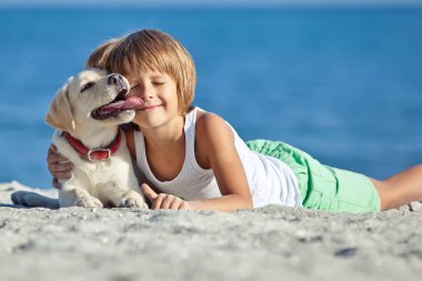 Mutlu çocuk mavi gökyüzüne karşı deniz kıyısında köpeğiyle oynuyor. En iyi arkadaşlar tatilde eğlenir..