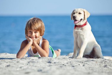 Mutlu çocuk mavi gökyüzüne karşı deniz kıyısında köpeğiyle oynuyor. En iyi arkadaşlar tatilde eğlenir..