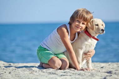 Mutlu çocuk mavi gökyüzüne karşı deniz kıyısında köpeğiyle oynuyor. En iyi arkadaşlar tatilde eğlenir..