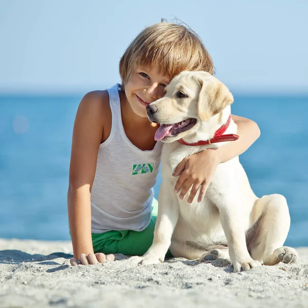 Happy boy playing with his dog on the seashore against the blue sky. Best friends have fun on vacation. — Stock Photo, Image