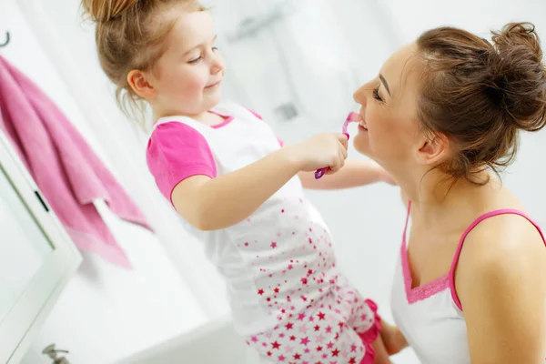 Мама з донькою чистять зуби зубними щітками у ванній кімнаті. Мама і маленька дівчинка в домашньому одязі.. — стокове фото