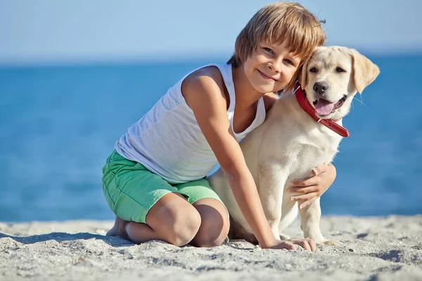 Happy boy playing with his dog on the seashore against the blue sky. Best friends have fun on vacation, play on the sand against the sea. — Stock Photo, Image