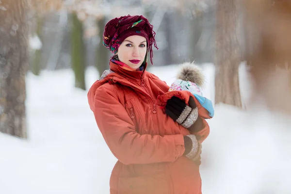 彼女の女の赤ちゃんを運ぶ母は赤いジャケットとスリングを着ています 冬の屋外の家族の楽しみを時間します — ストック写真