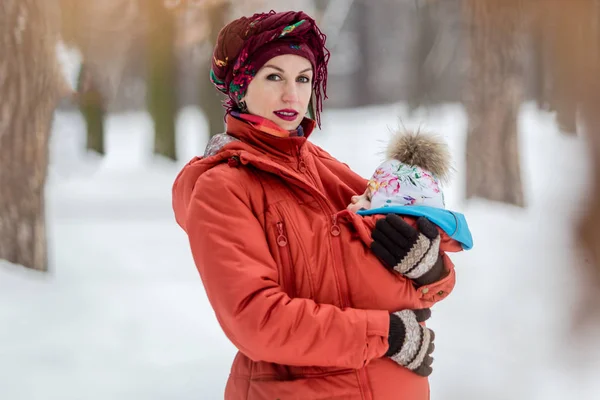 Mãe carregando seu bebê menina usa jaqueta vermelha e funda . — Fotografia de Stock