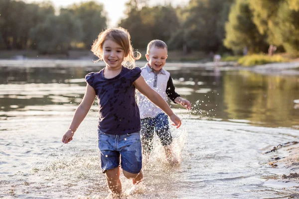Två lyckliga barn som springer genom vattnet på sommaren — Stockfoto
