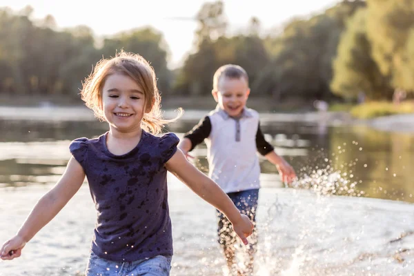Zwei glückliche Kinder, die im Sommer durchs Wasser laufen — Stockfoto