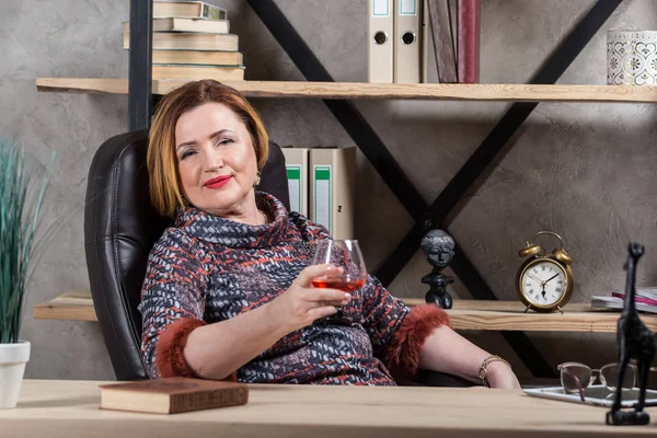 Senior zakenvrouw ontspannen op stoel met wijn. — Stockfoto
