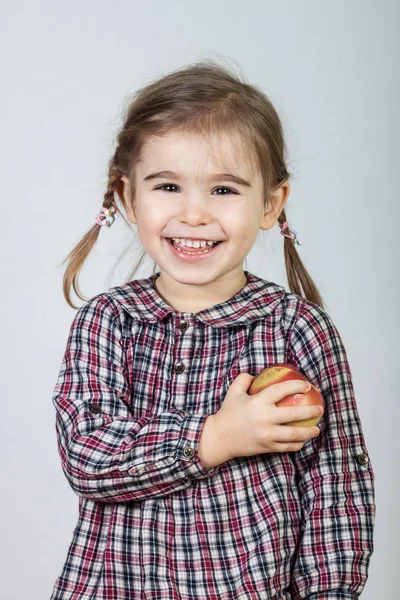 Menina feliz se divertindo e comendo maçã no fundo cinza — Fotografia de Stock