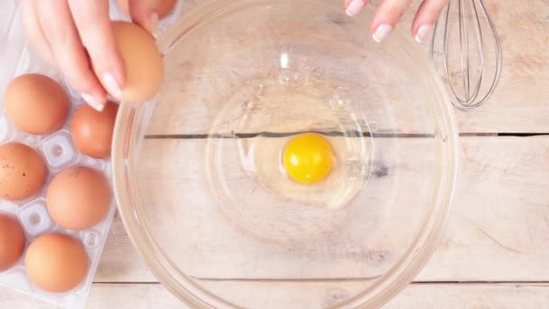 女性の手はボウルに卵を割り 泡立て器でそれらを混合する — ストック動画