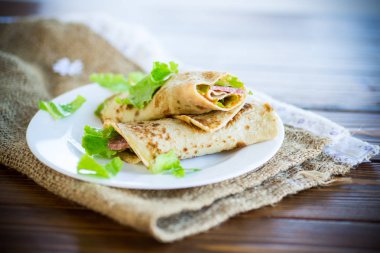 salata yaprakları ve ahşap bir masa üzerinde bir tabak içinde pastırma ile ince krep