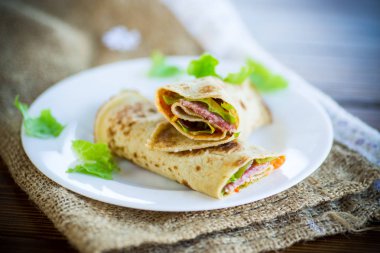 salata yaprakları ve ahşap bir masa üzerinde bir tabak içinde pastırma ile ince krep