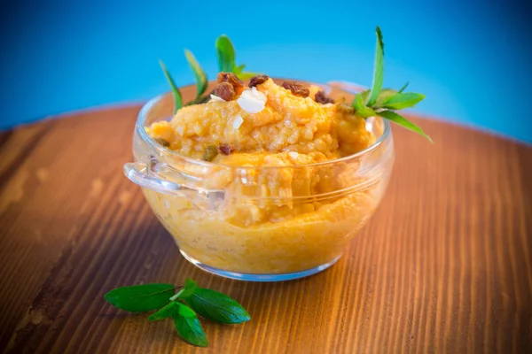 boiled sweet pumpkin porridge with raisins and nuts in a glass bowl on a blue background