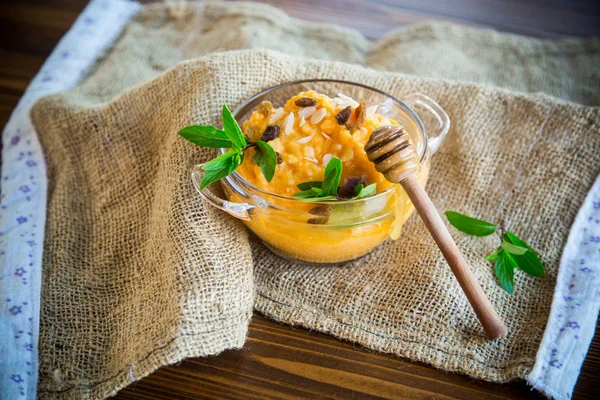 boiled sweet pumpkin porridge with raisins and nuts in a glass bowl on wooden background